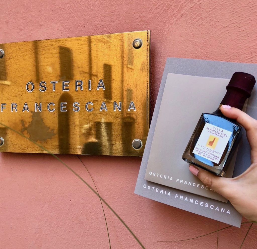 Bottle of balsamic vinegar being held by the Osteria Francescana sign