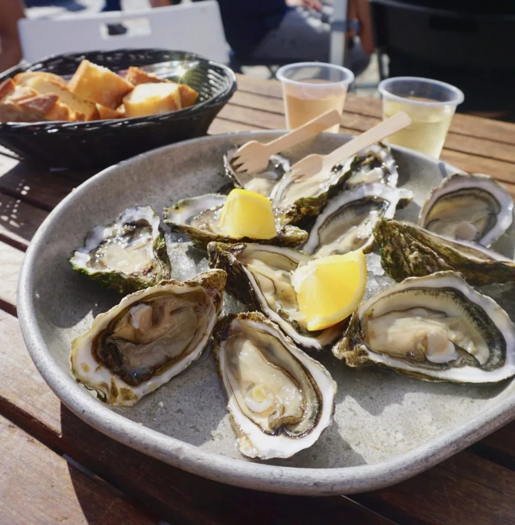 Tray of oysters with a bread basket and two glasses of wine