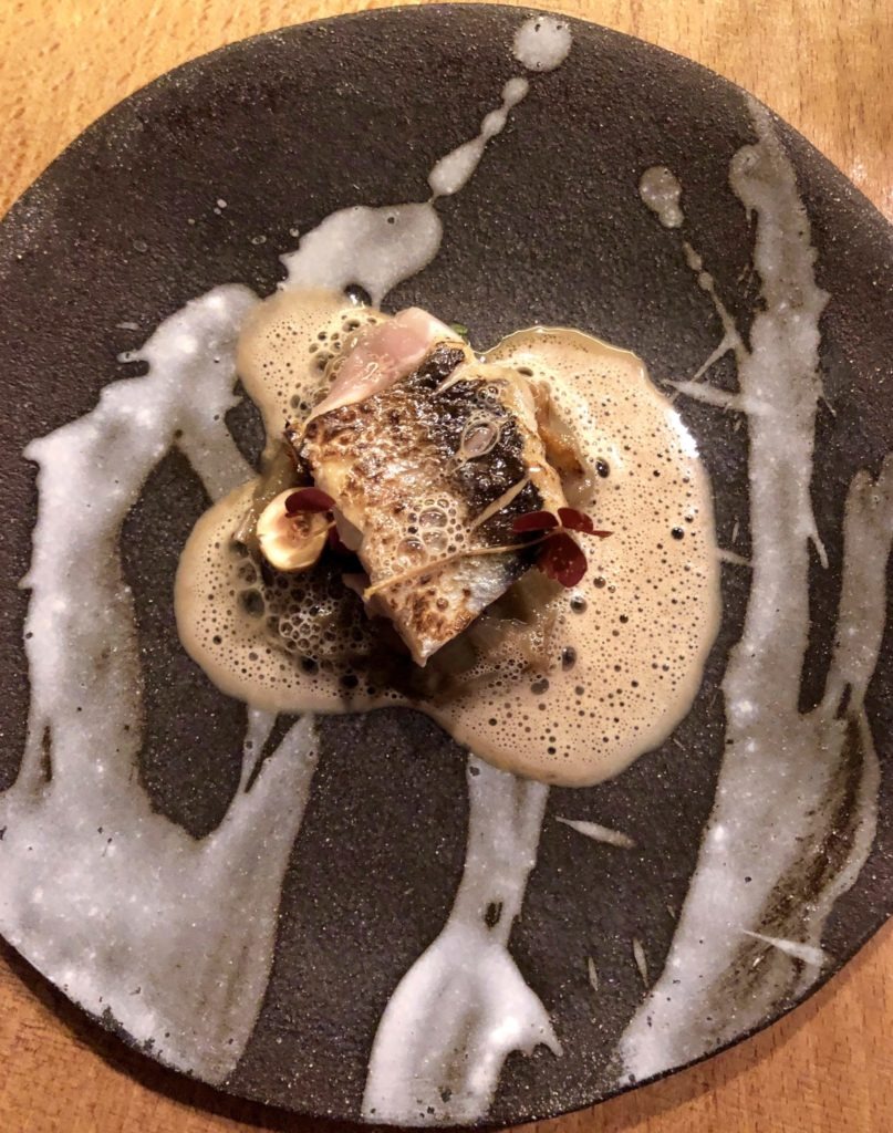 Black and white plate topped with fish and foam sauce