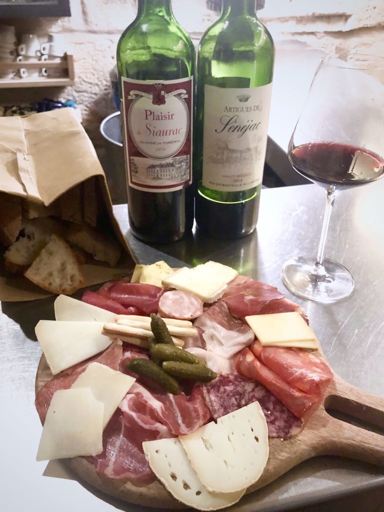 Cheese and charcuterie on a platter with two wine bottles and bread