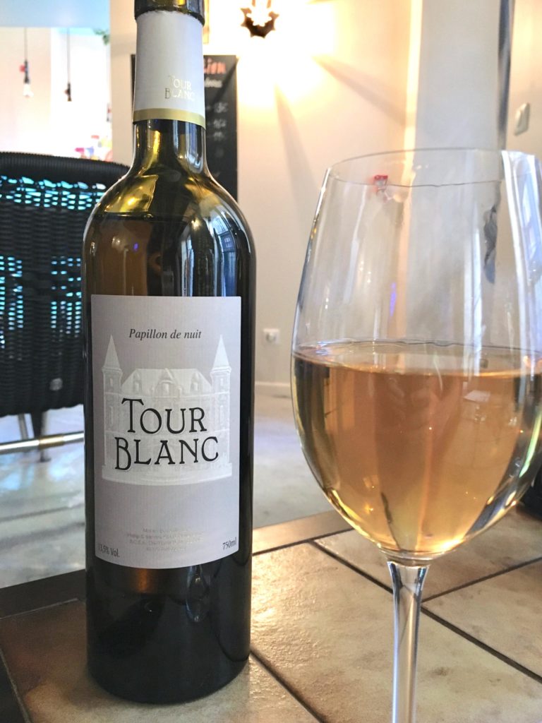 Glass of ugni blanc in front of Tour Blanc wine bottle