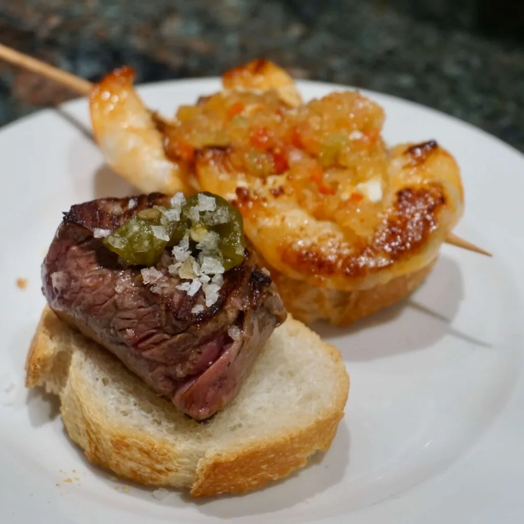 Veal tenderloin on bread, topped with a roasted green pepper and sea salt along with 3 grilled prawns on a skewer atop bread with peppers and onion from Gandarias in San Sebastián.