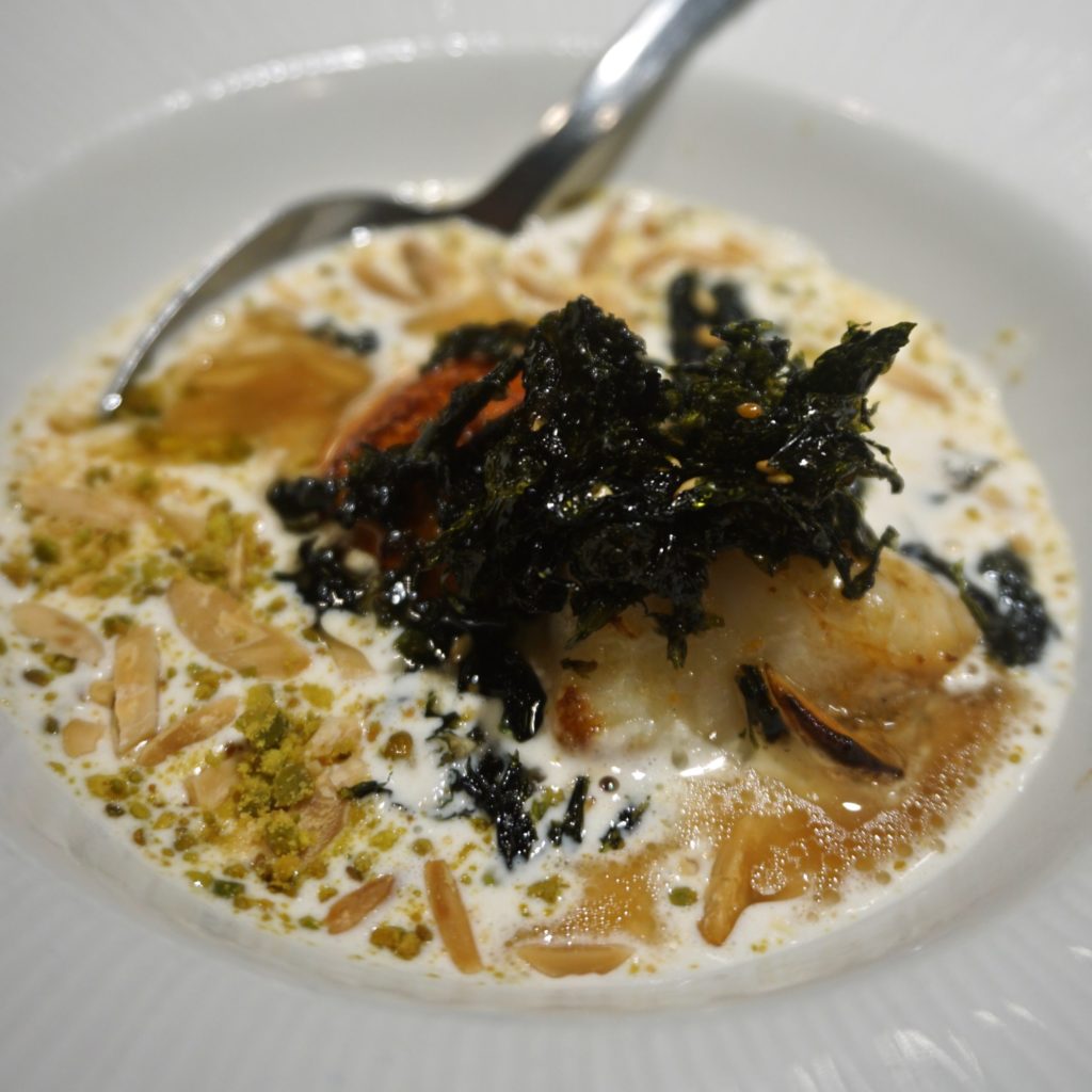 White dish filled with scallops, white cream, almonds, oil, and seaweed