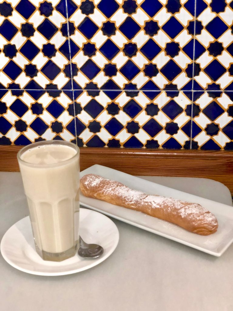 Glass of horchata on white plate next to a farton on a plate with blue and white tiled background