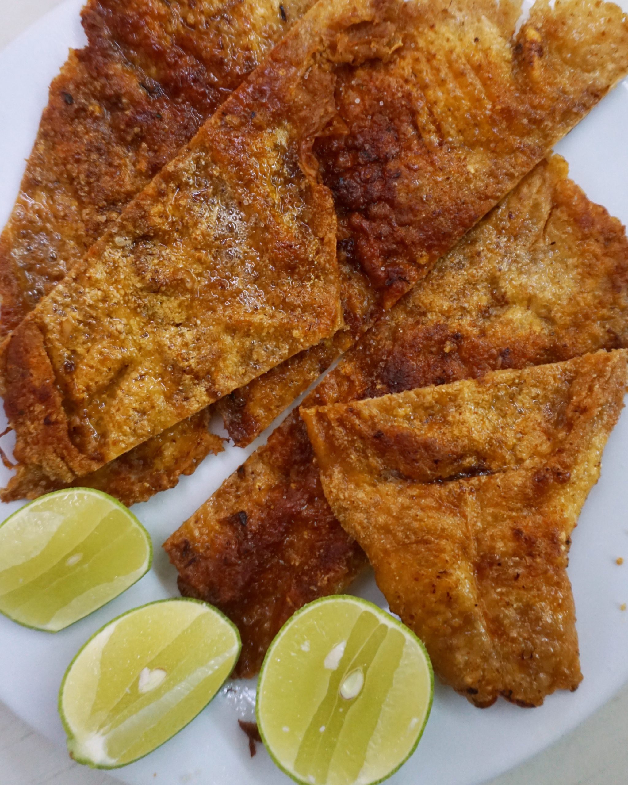 Fried turkey skin on a white plate with three limes
