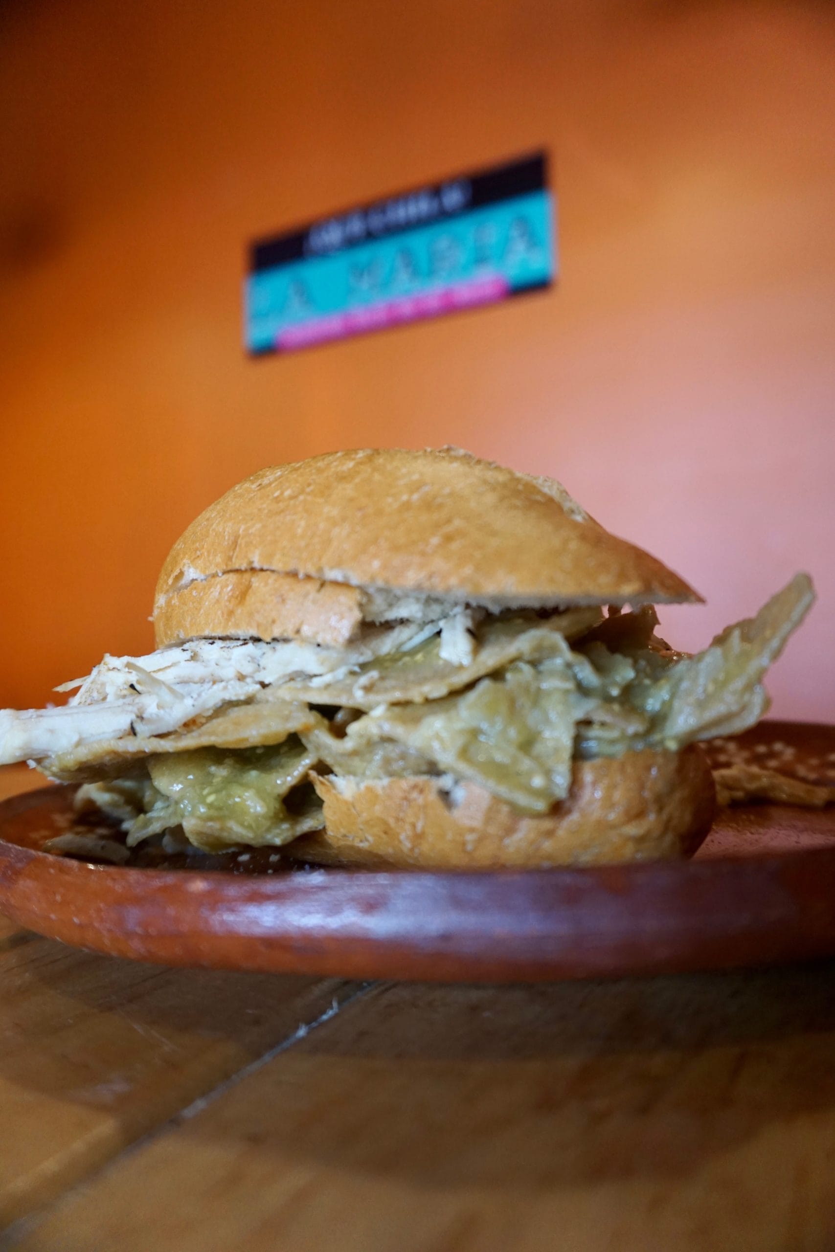 A torta filled with green chilaquiles on a plate with an orange background