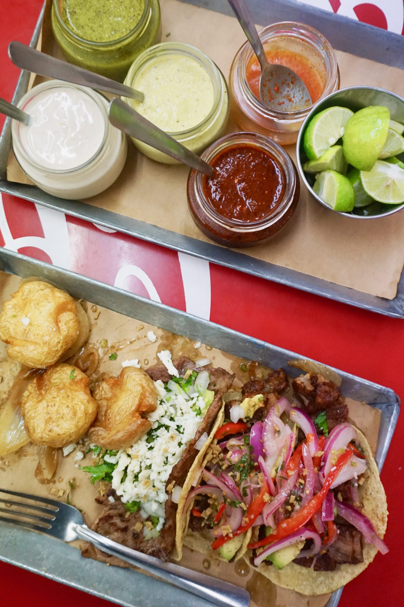 three tacos on a tray next to a tray of salsas