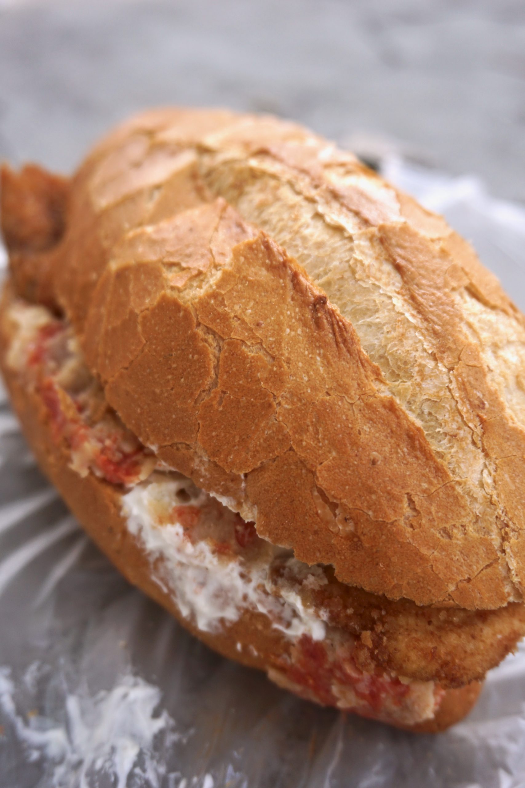 Torta filled with red chilaquiles, sour cream, and chicken milanese on a plastic wrapper