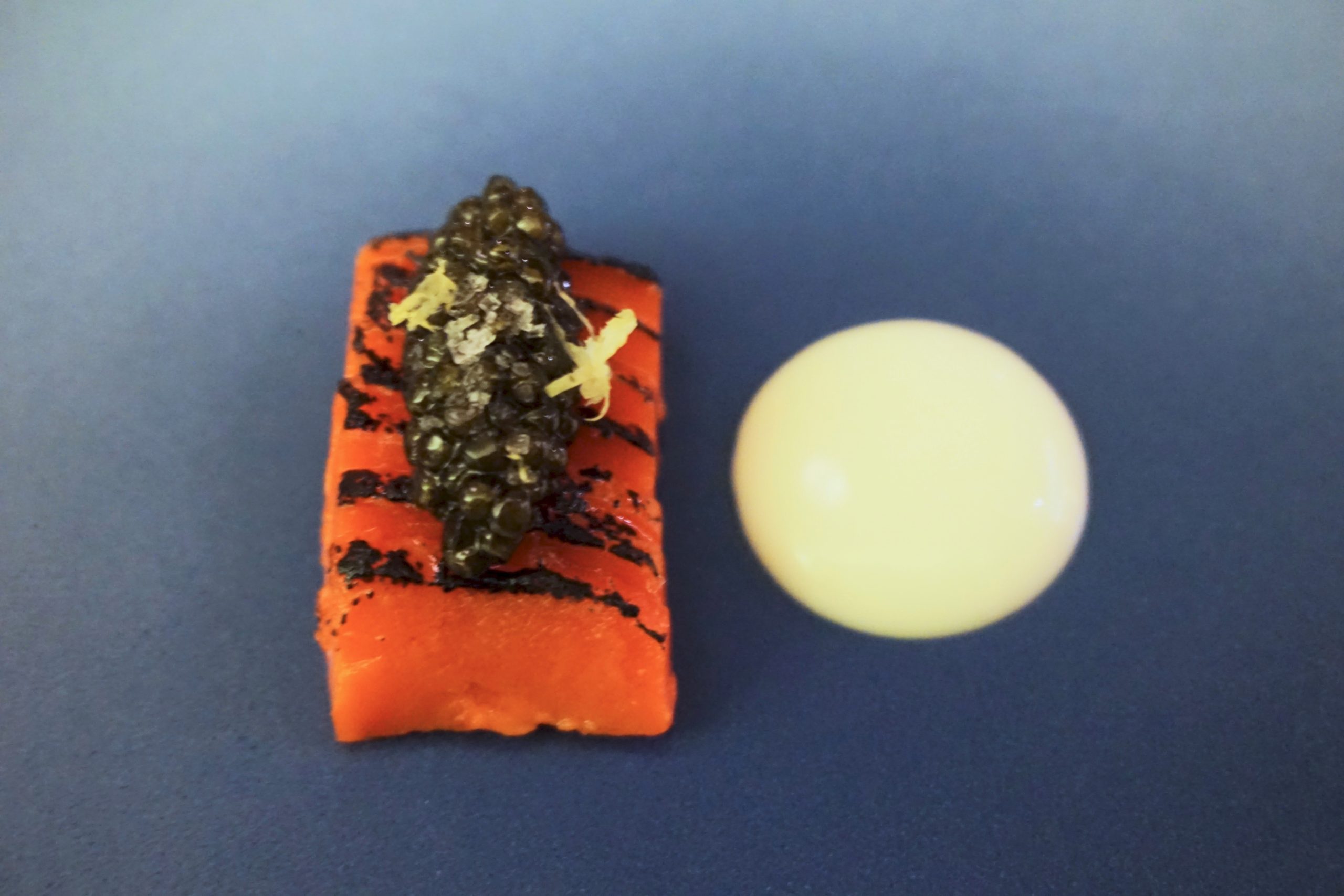 Blue plate topped with slices of papaya and caviar with a circle of cream