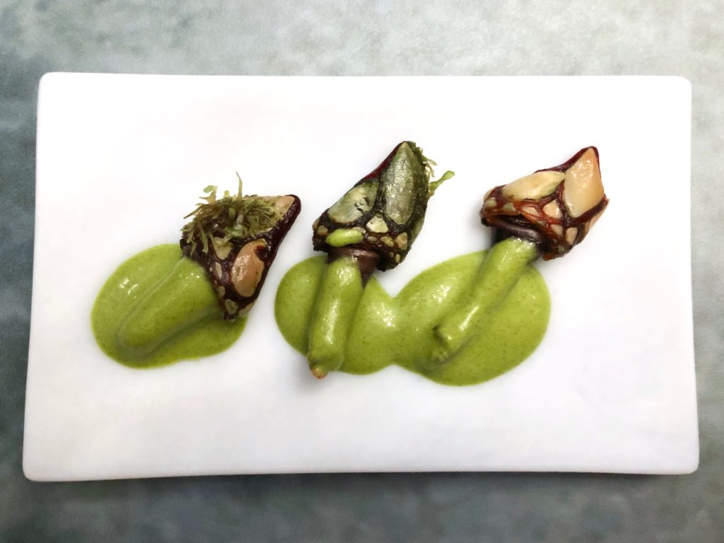 Three percebes on a white plate with a green sauce