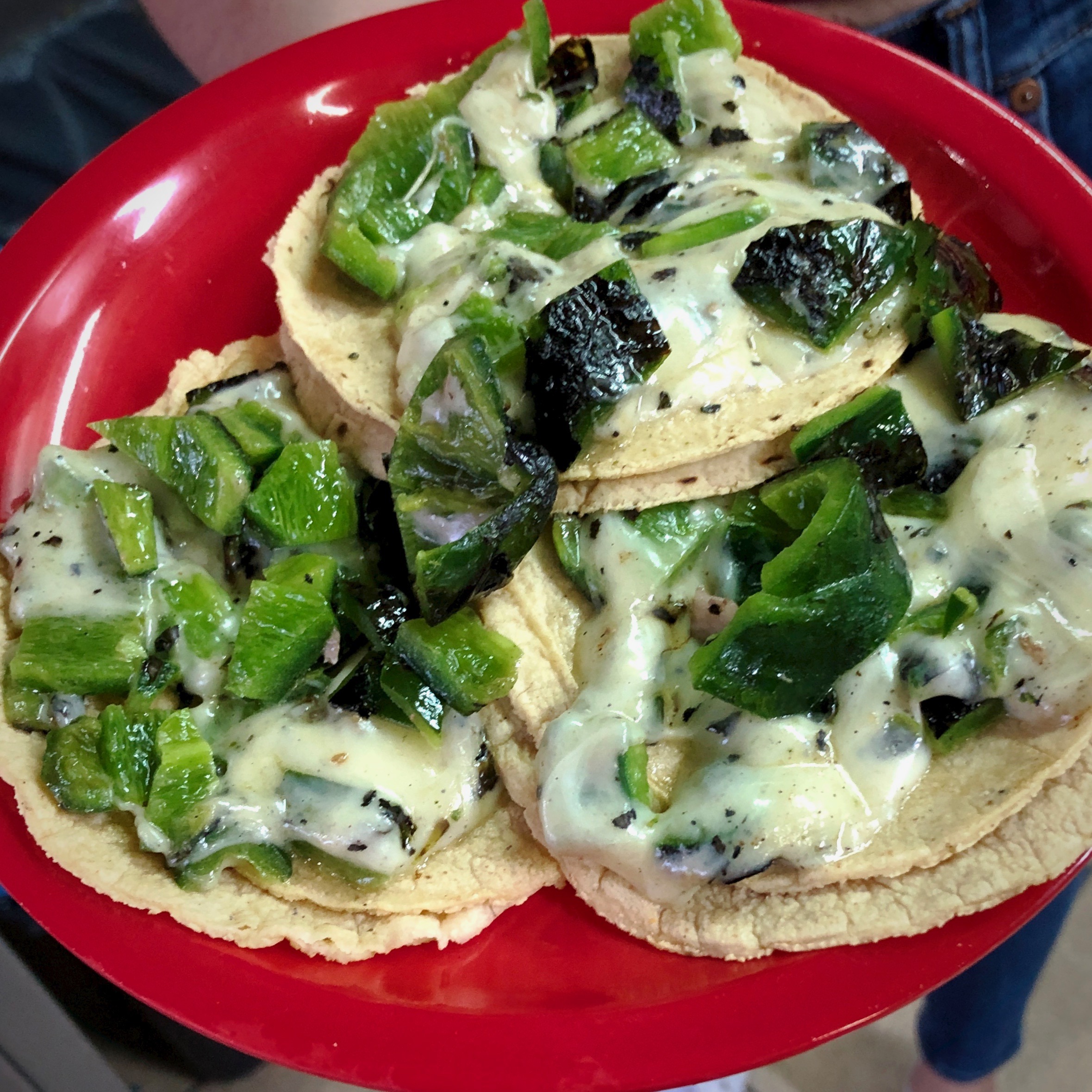 Three tacos with roasted poblano pepper pieces and melted cheese on a red plate