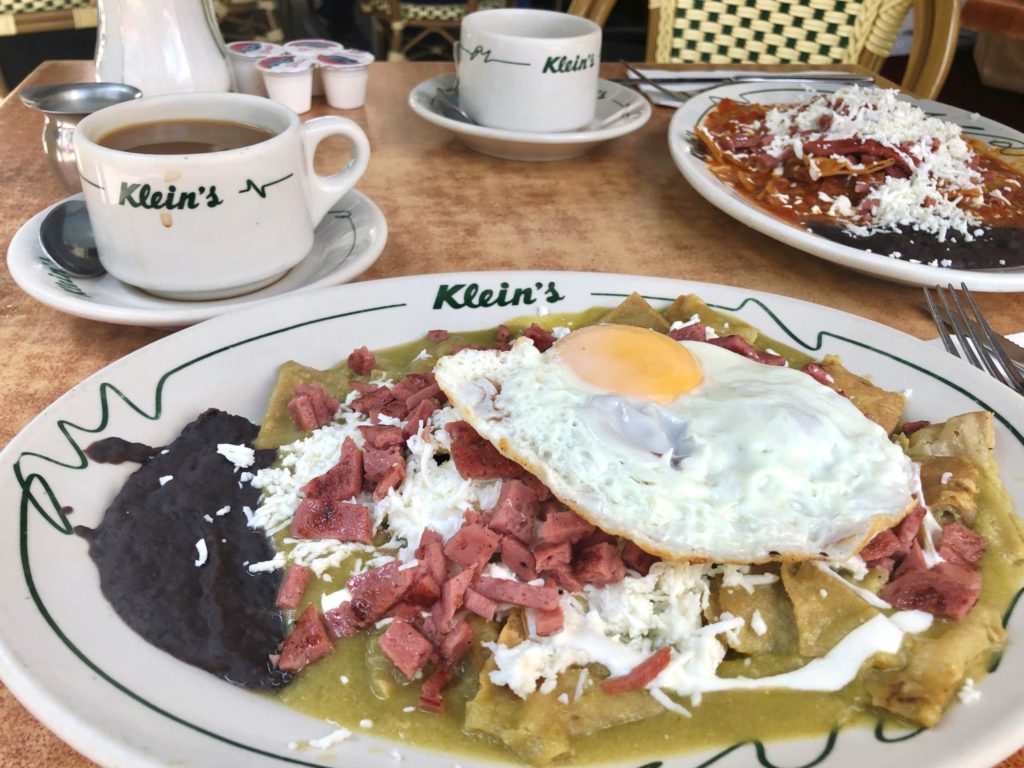 Plate of chilaquiles with green salsa and salami topped with an egg and side of refried black beans