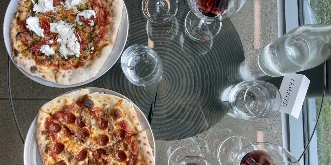 Two pizzas on table with glasses of red wine