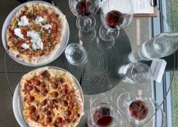Two pizzas on table with glasses of red wine