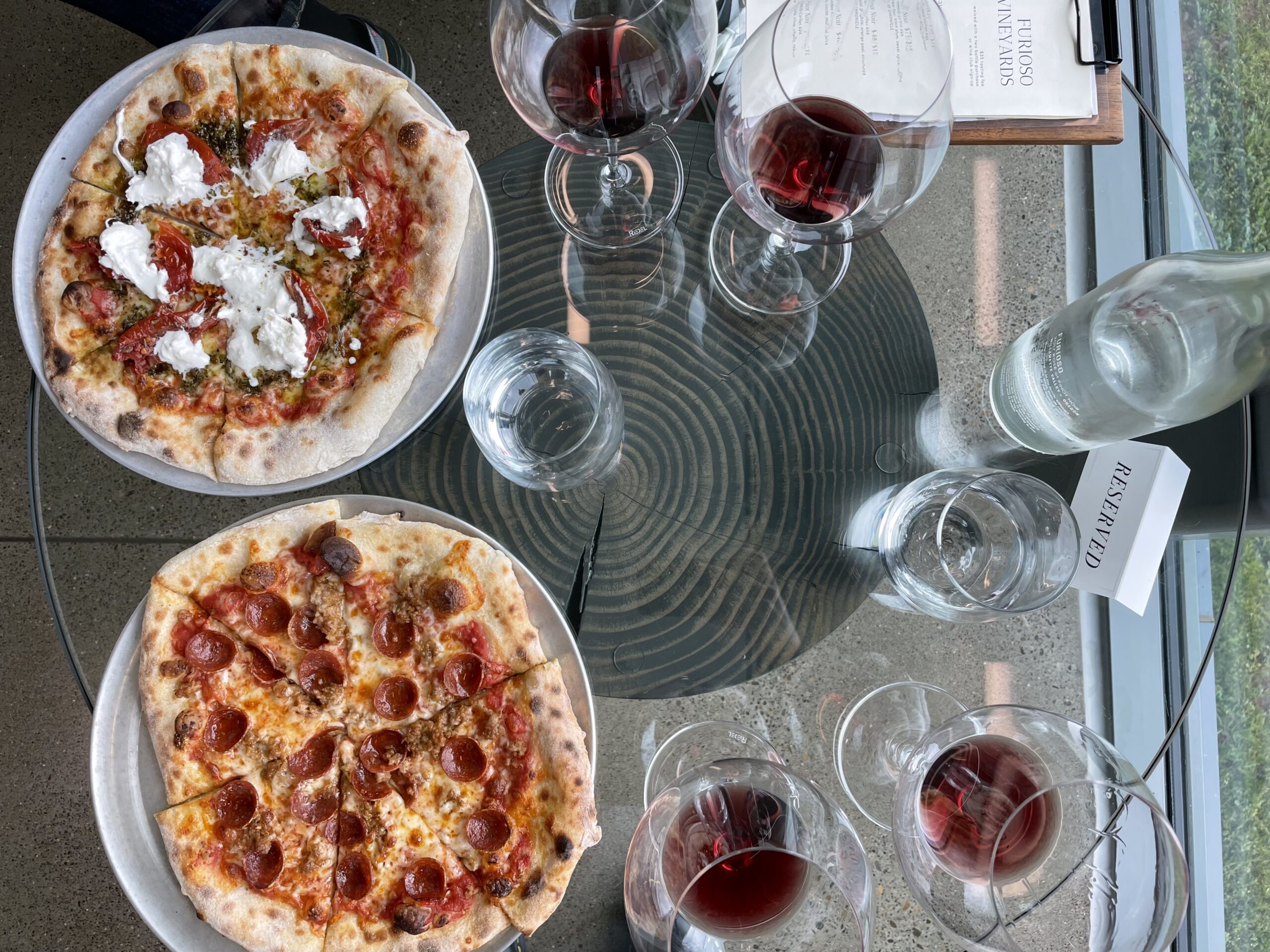Two pizzas on table with glasses of red wine