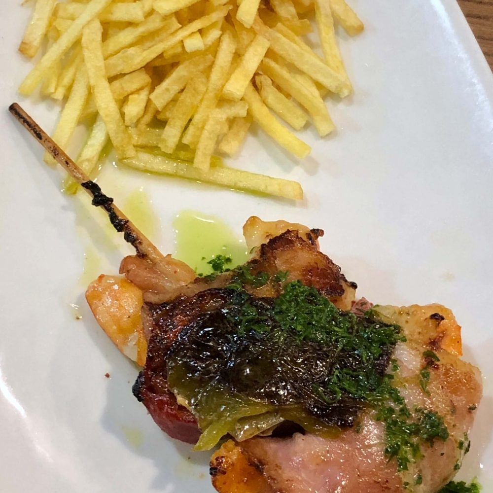 A skewer of king prawn wrapped in bacon and served with crispy potato sticks from Casa Senra Donostia.